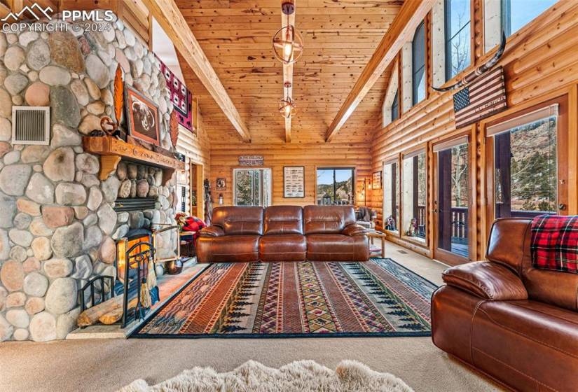 Carpeted living room with beamed ceiling, log walls, high vaulted ceiling, wood ceiling, and a stone fireplace