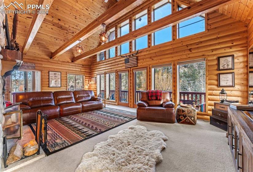 Carpeted living room with beam ceiling, log walls, wooden ceiling, and high vaulted ceiling