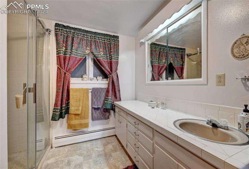 Bathroom featuring a shower with curtain, dual bowl vanity, a baseboard heating unit, and tile flooring