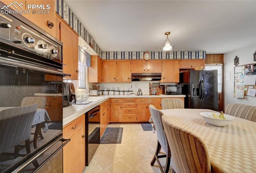 Kitchen featuring backsplash, black appliances, sink, decorative light fixtures, and tile countertops