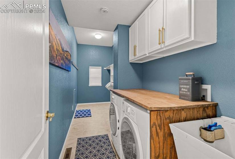 Laundry room with light tile floors, washing machine and dryer, and cabinets