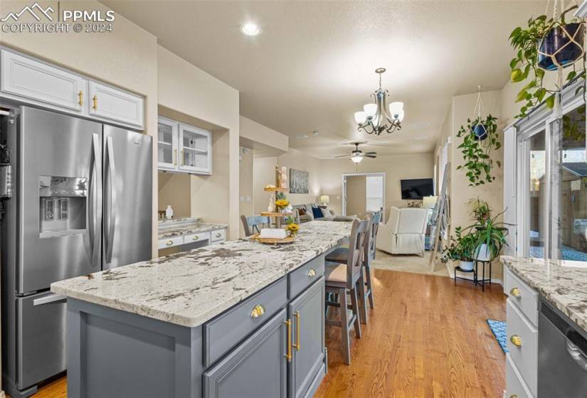 Kitchen with light wood-type flooring, ceiling fan with notable chandelier, stainless steel appliances, white cabinetry, and a kitchen island
