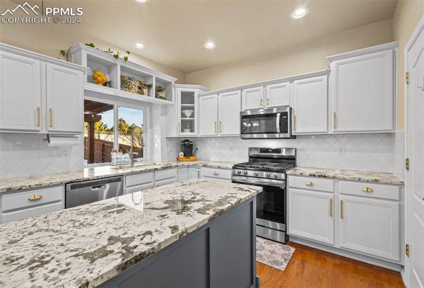Kitchen with stainless steel appliances, white cabinets, tasteful backsplash, light hardwood / wood-style flooring, and sink