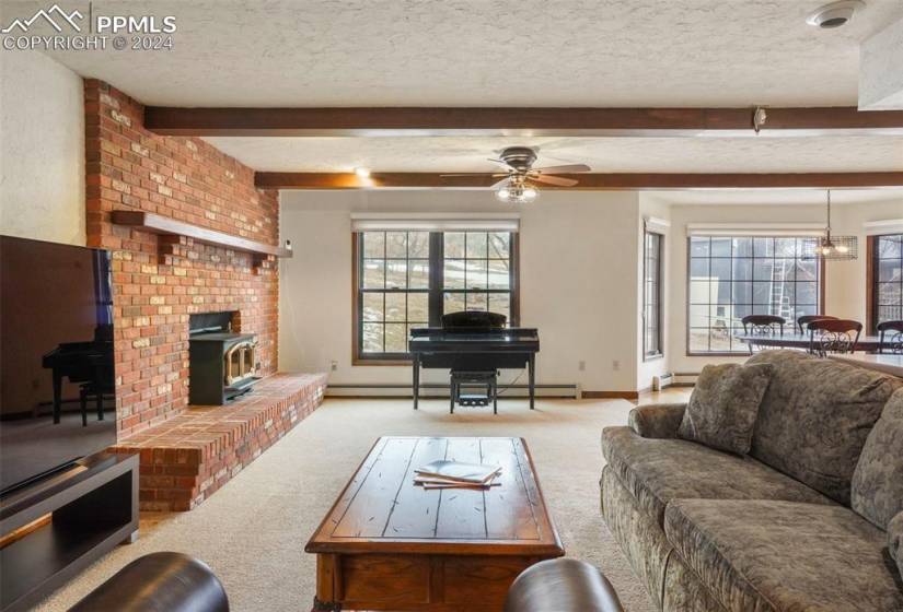 Carpeted living room with brick wall, ceiling fan, a textured ceiling, and beam ceiling
