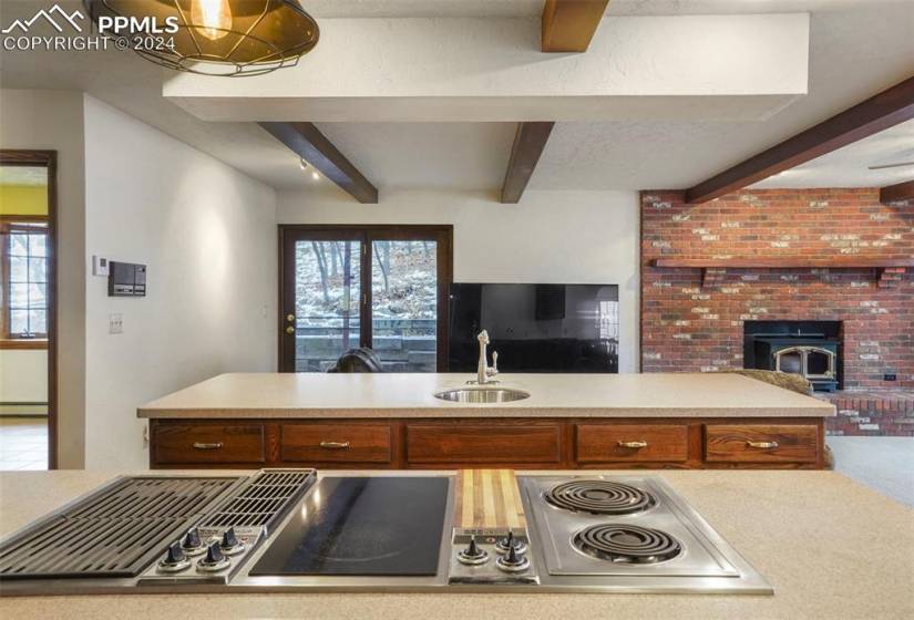 Kitchen featuring stainless steel electric stovetop, carpet floors, sink, a brick fireplace, and beam ceiling