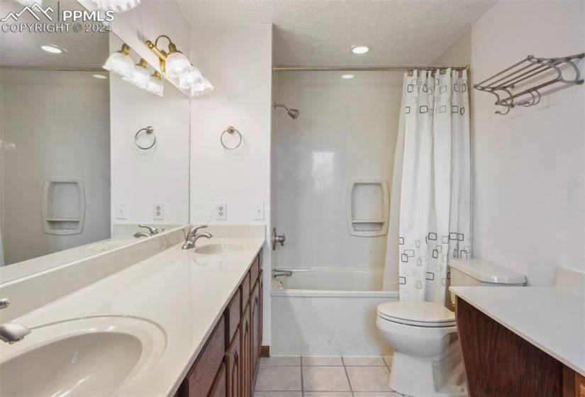 Full, Pass-through bathroom with oversized vanity, a textured ceiling, toilet, shower / bathtub combination with curtain, and tile flooring