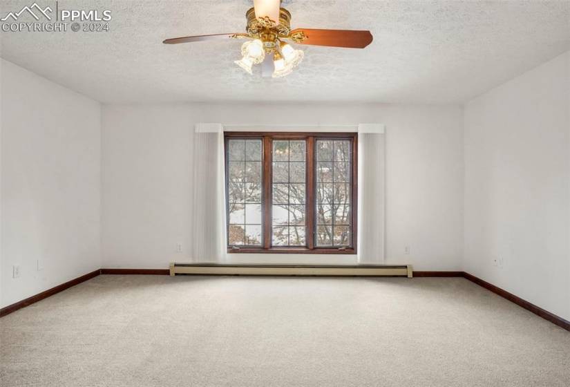 Carpeted empty room featuring a baseboard heating unit, ceiling fan, and a textured ceiling