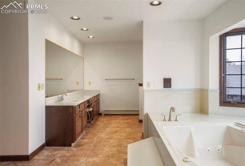 Bathroom featuring a baseboard radiator, tile flooring, a bath to relax in, and vanity with extensive cabinet space