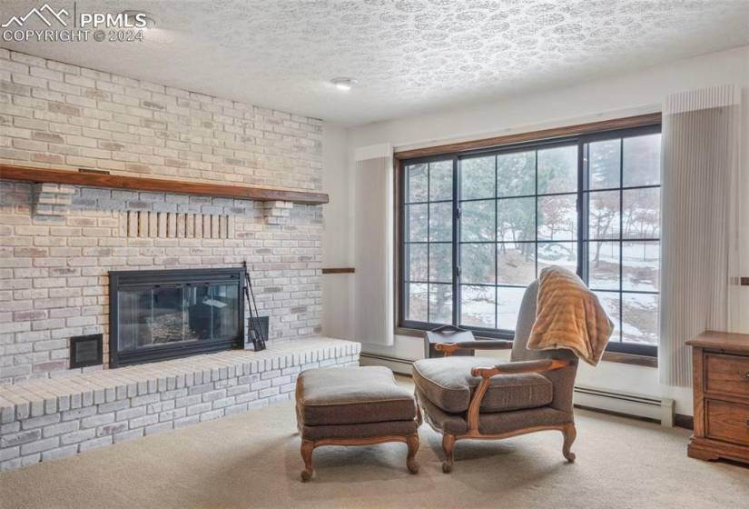 Sitting area featuring a baseboard radiator, light colored carpet, a brick fireplace, and a textured ceiling