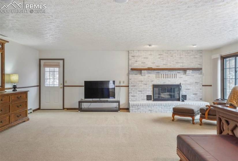 Carpeted living room with a brick fireplace, a textured ceiling, and a healthy amount of sunlight