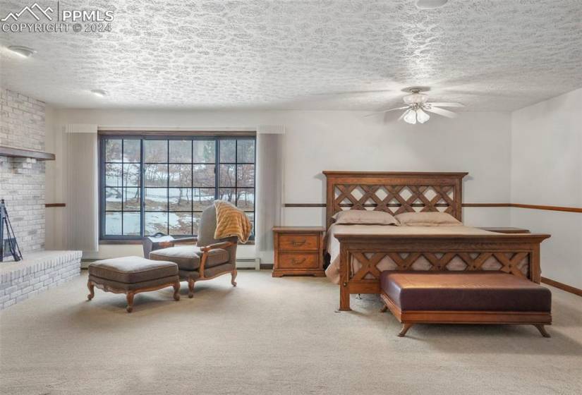 Bedroom featuring a brick fireplace, ceiling fan, light colored carpet, and a textured ceiling