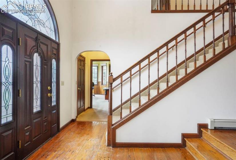 Foyer entrance featuring hardwood / wood-style flooring, a baseboard radiator, and a towering ceiling