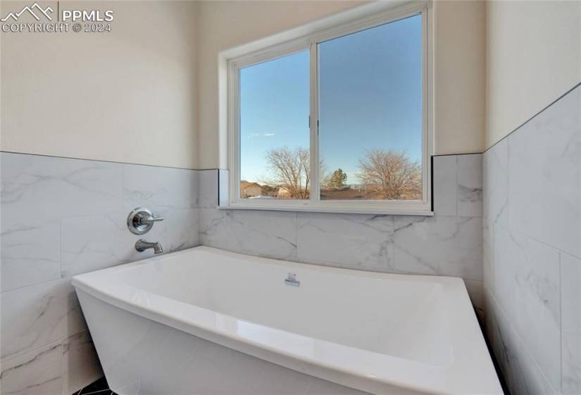 Bathroom featuring plenty of natural light, a bathtub, and tile walls