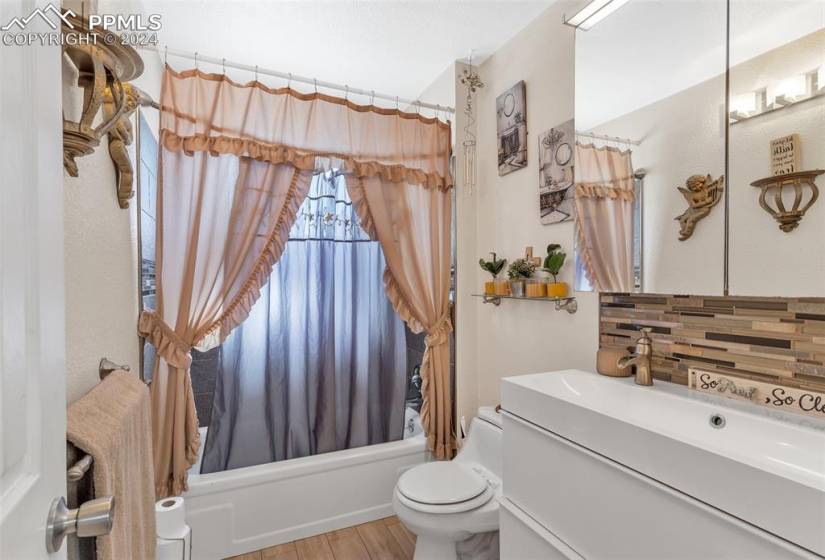 Full upper bathroom with hardwood / wood-style floors, oversized vanity, backsplash, toilet, and shower / bath combination with curtain
