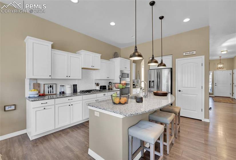 Kitchen featuring light wood-type flooring, stainless steel appliances, a kitchen island with sink, and white cabinetry