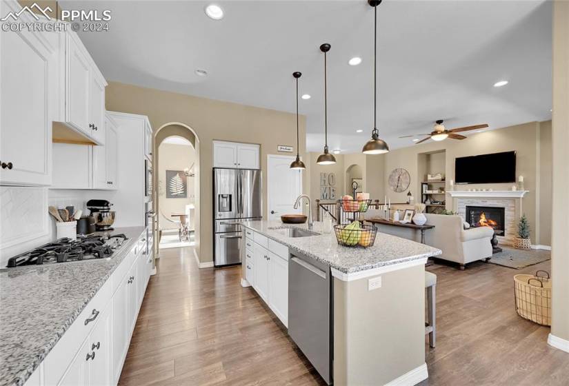 Kitchen featuring a stone fireplace, stainless steel appliances, a kitchen island with sink, and light wood-type flooring