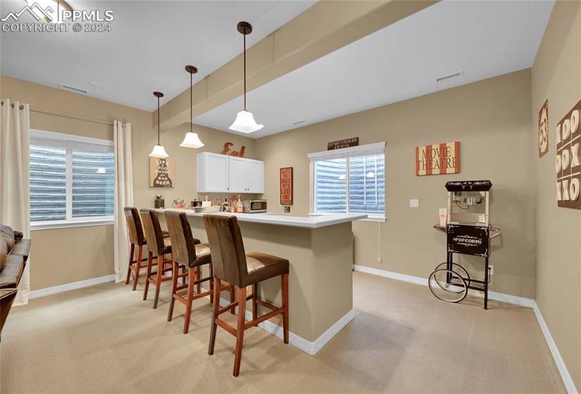 Kitchen with pendant lighting, white cabinetry, a breakfast bar, beamed ceiling, and light carpet