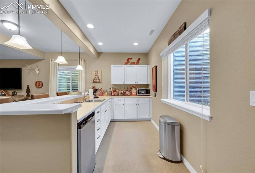 Kitchen featuring white cabinetry, sink, stainless steel appliances, decorative light fixtures, and light carpet