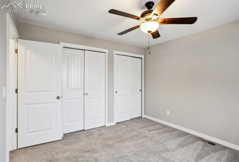 Unfurnished bedroom featuring multiple closets, ceiling fan, and light colored carpet