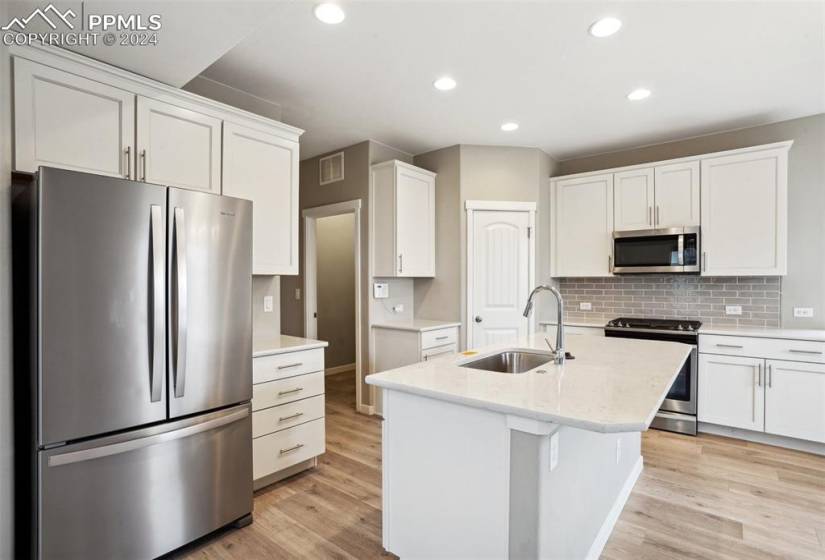 Kitchen featuring stainless steel appliances, white cabinetry, light hardwood / wood-style flooring, a kitchen island with sink, and sink
