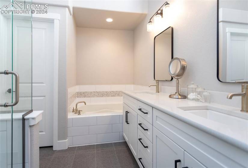Bathroom with tiled tub, double vanity, and tile flooring
