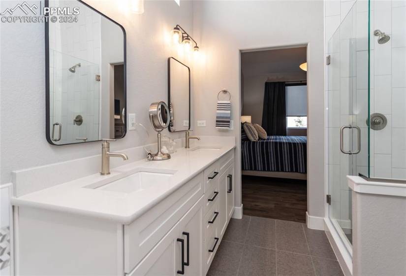 Bathroom with double vanity, a shower with shower door, and tile floors