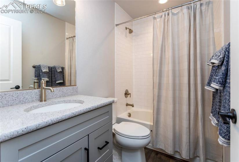 Full bathroom with shower / bathtub combination with curtain, toilet, hardwood / wood-style floors, and vanity with extensive cabinet space