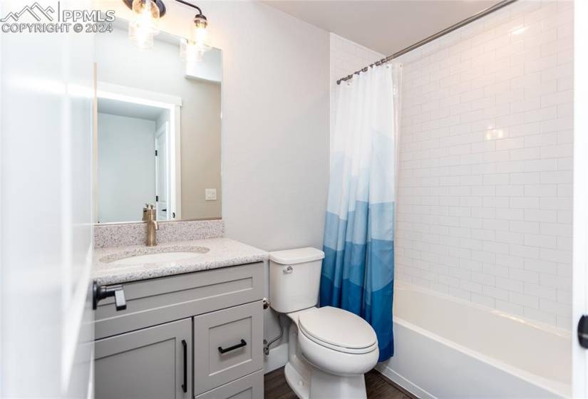Full bathroom with large vanity, wood-type flooring, shower / tub combo with curtain, and toilet