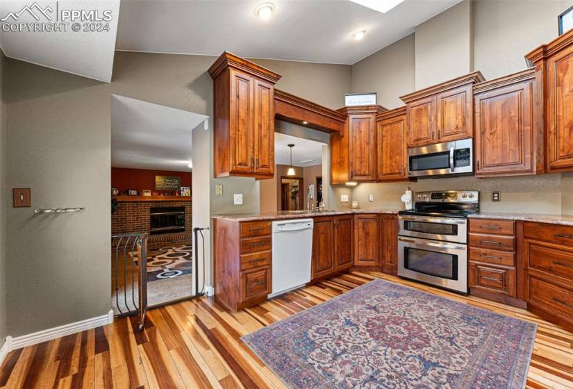 Kitchen with lofted ceiling, stainless steel appliances, light stone counters, and light wood-type flooring
