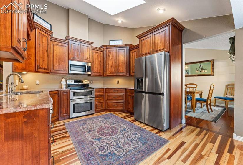 Kitchen featuring light wood-type flooring, stainless steel appliances, high vaulted ceiling, a skylight, and sink