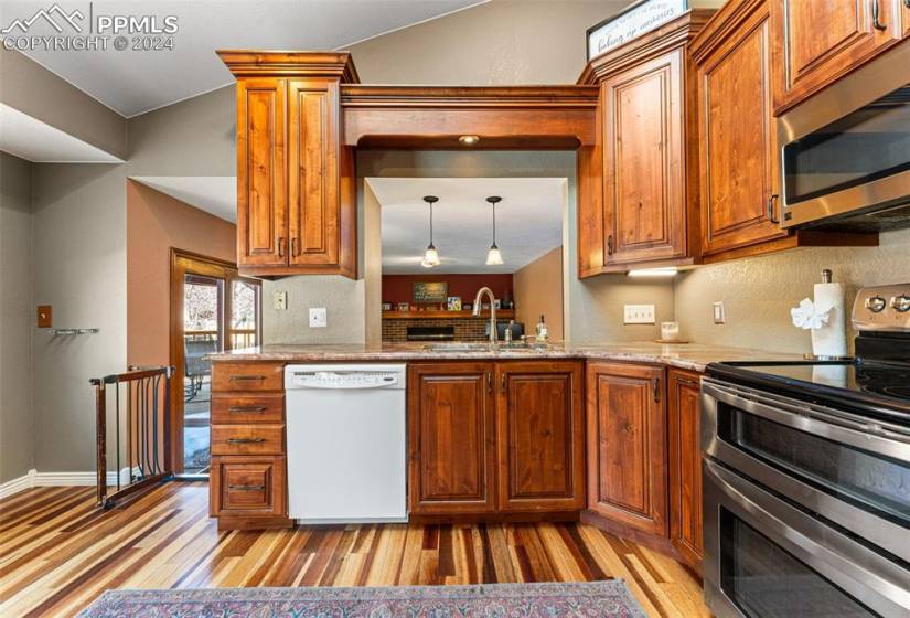 Kitchen featuring stainless steel appliances, light stone counters, light hardwood / wood-style floors, sink, and decorative light fixtures