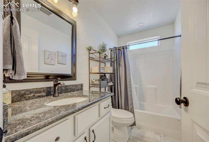 Full bathroom featuring shower / bath combo with shower curtain, vanity, a textured ceiling, toilet, and tile flooring