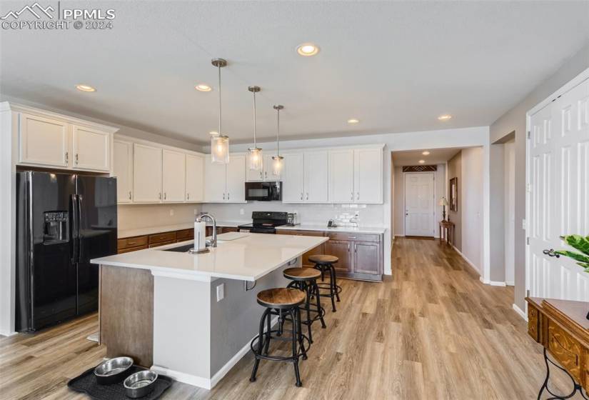 Kitchen featuring a center island with sink, light hardwood / wood-style flooring, black appliances, and white cabinetry