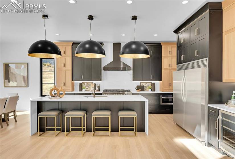 Kitchen featuring light wood-type flooring, wall chimney range hood, an island with sink, and stainless steel appliances