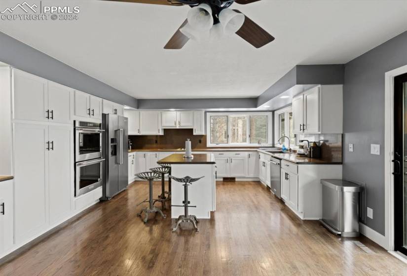 Kitchen featuring hardwood flooring, stainless steel appliances, ceiling fan, and white cabinetry. with new doors.