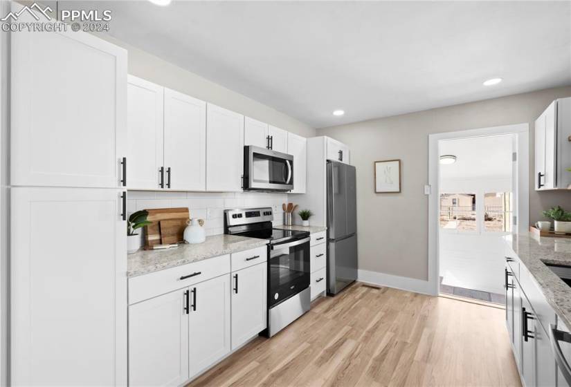 Kitchen featuring light hardwood / wood-style flooring, light stone counters, white cabinets, tasteful backsplash, and appliances with stainless steel finishes