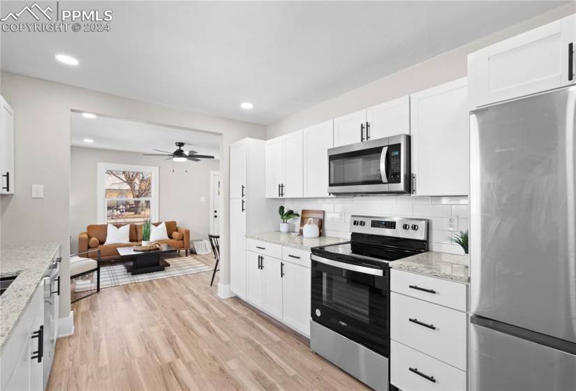 Kitchen with light hardwood / wood-style floors, white cabinets, ceiling fan, tasteful backsplash, and appliances with stainless steel finishes