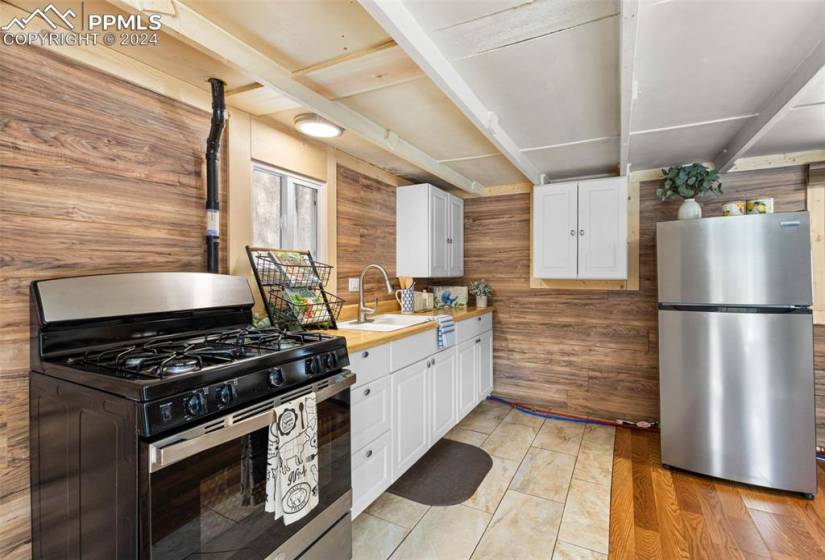 Kitchen with stainless steel appliances, white cabinets, light hardwood / wood-style flooring, sink, and wood walls