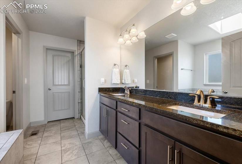 Primary Owner's Bathroom w/ tile floor, dual sink vanity, separate shower, soaking tub, and walk-in closet.