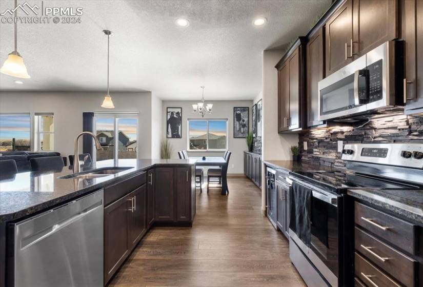 The kitchen is a chef's delight, featuring a pantry, counter bar w/ pendant lights, espresso cabinets w/ granite countertops, & stainless-steel appliances.