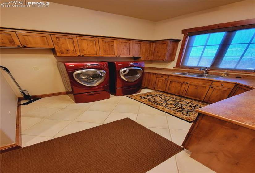 Laundry/ Mudroom featuring lots of cabinet storage, light tile flooring, sink, coat rack storage with bench seating on opposite wall.
