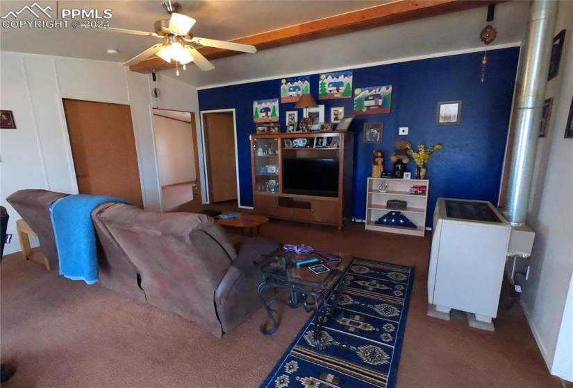 Living room with dark colored carpet, ceiling fan, and vaulted ceiling with beams