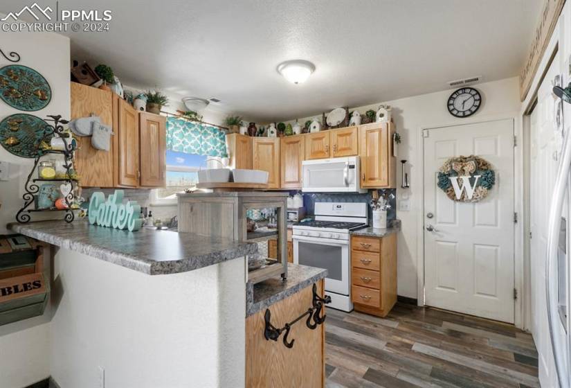 Kitchen featuring white appliances, light brown cabinets, dark hardwood / wood-style floors, and backsplash