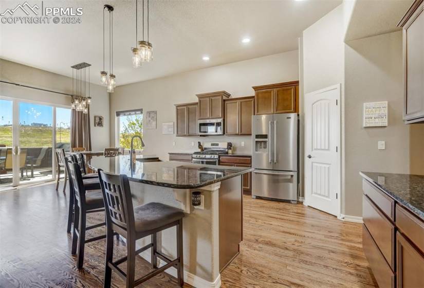 Kitchen featuring a notable chandelier, light wood-type flooring, decorative light fixtures, stainless steel appliances, and a kitchen island with sink