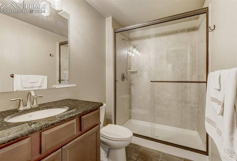 Bathroom featuring an enclosed shower, toilet, tile floors, and vanity with extensive cabinet space