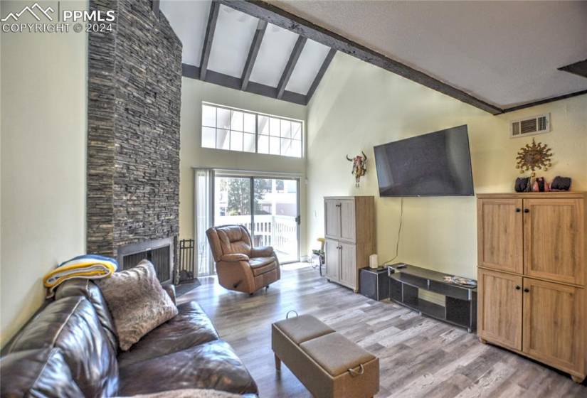Living room with a stone fireplace, beam ceiling, light hardwood / wood-style floors, and high vaulted ceiling