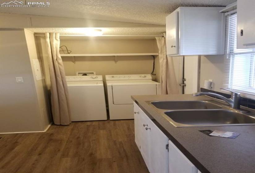 Clothes washing area featuring dark wood-type flooring, washing machine and dryer, a textured ceiling, washer hookup, and sink