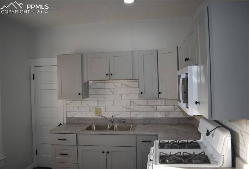 Kitchen featuring tasteful backsplash, white gas stove, sink, and gray cabinetry