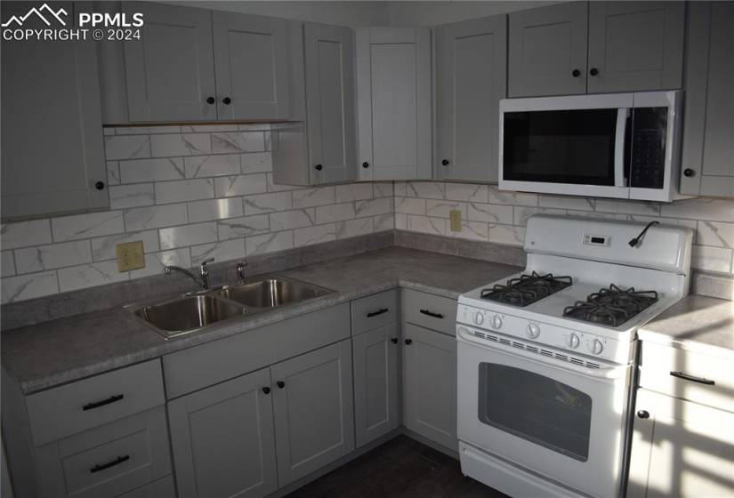 Kitchen featuring dark wood-type flooring, white gas stove, sink, and backsplash