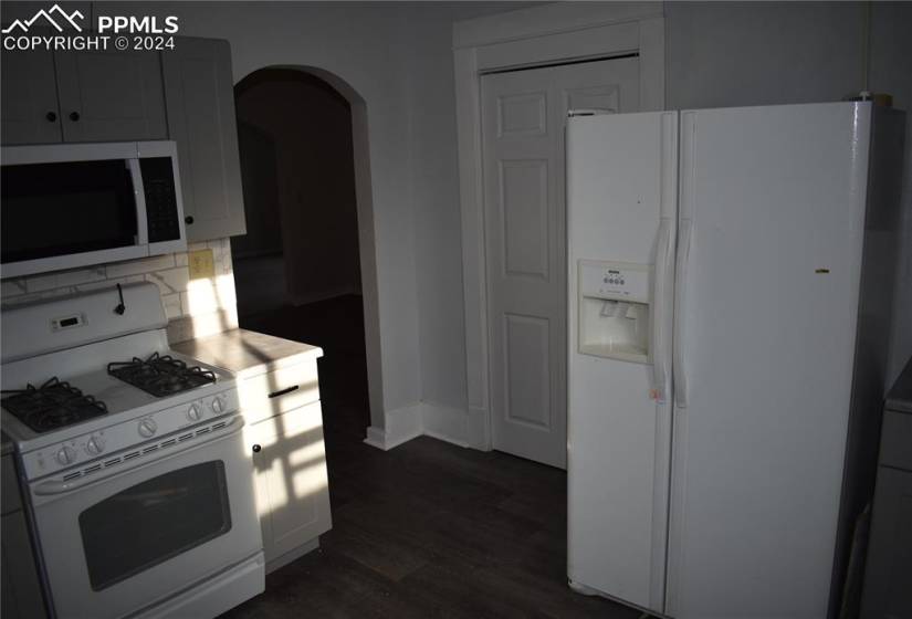 Kitchen with tasteful backsplash, white appliances, and dark wood-type flooring